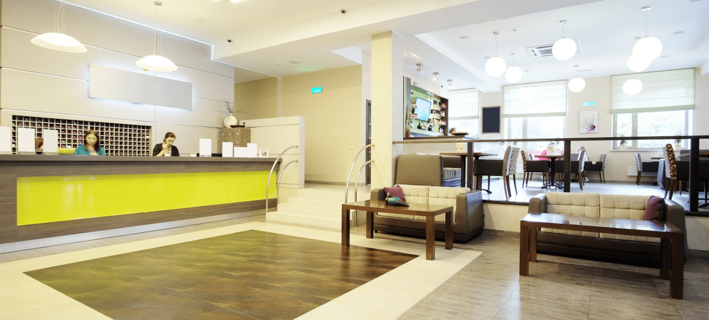 A hotel lobby with a lime green reception desk, seating area and dining tables beyond